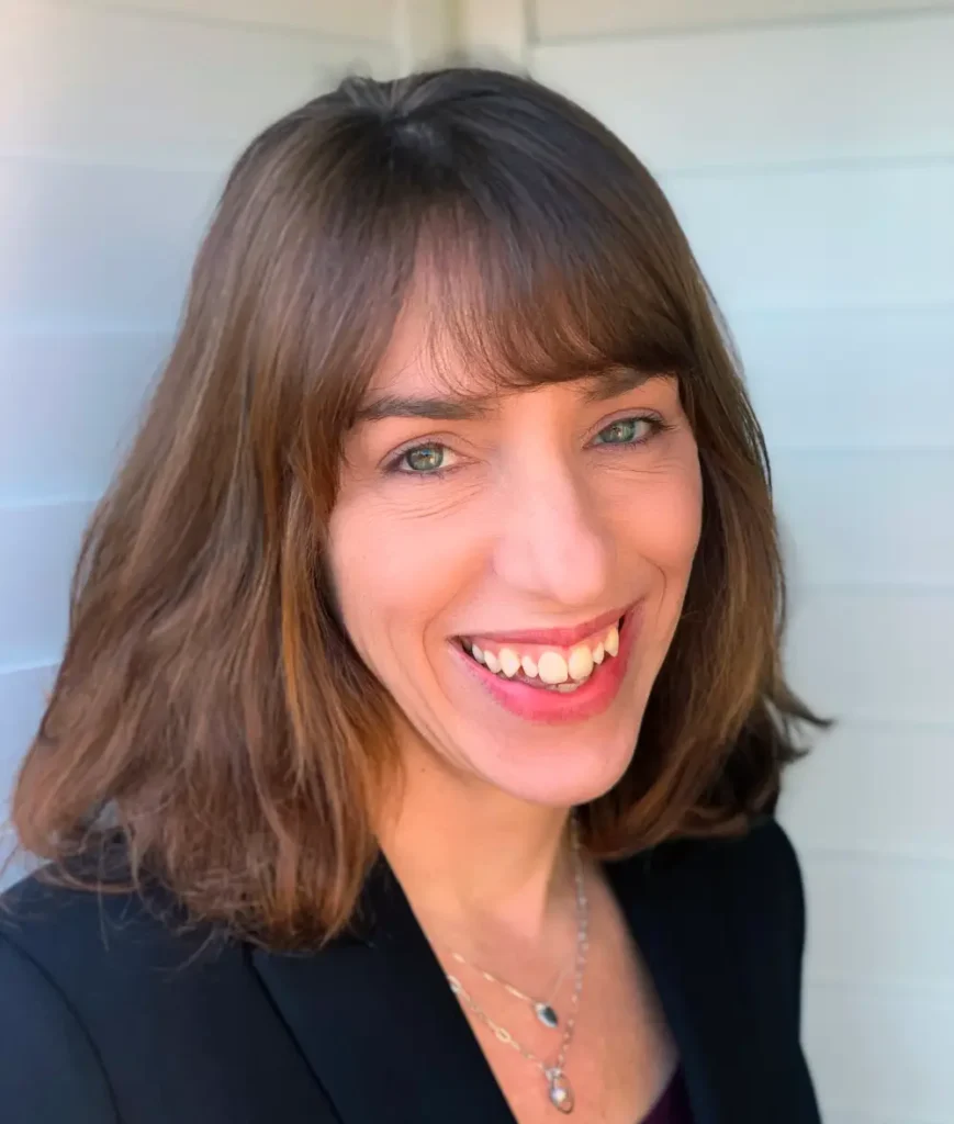 A woman with brown hair and blue eyes smiling.